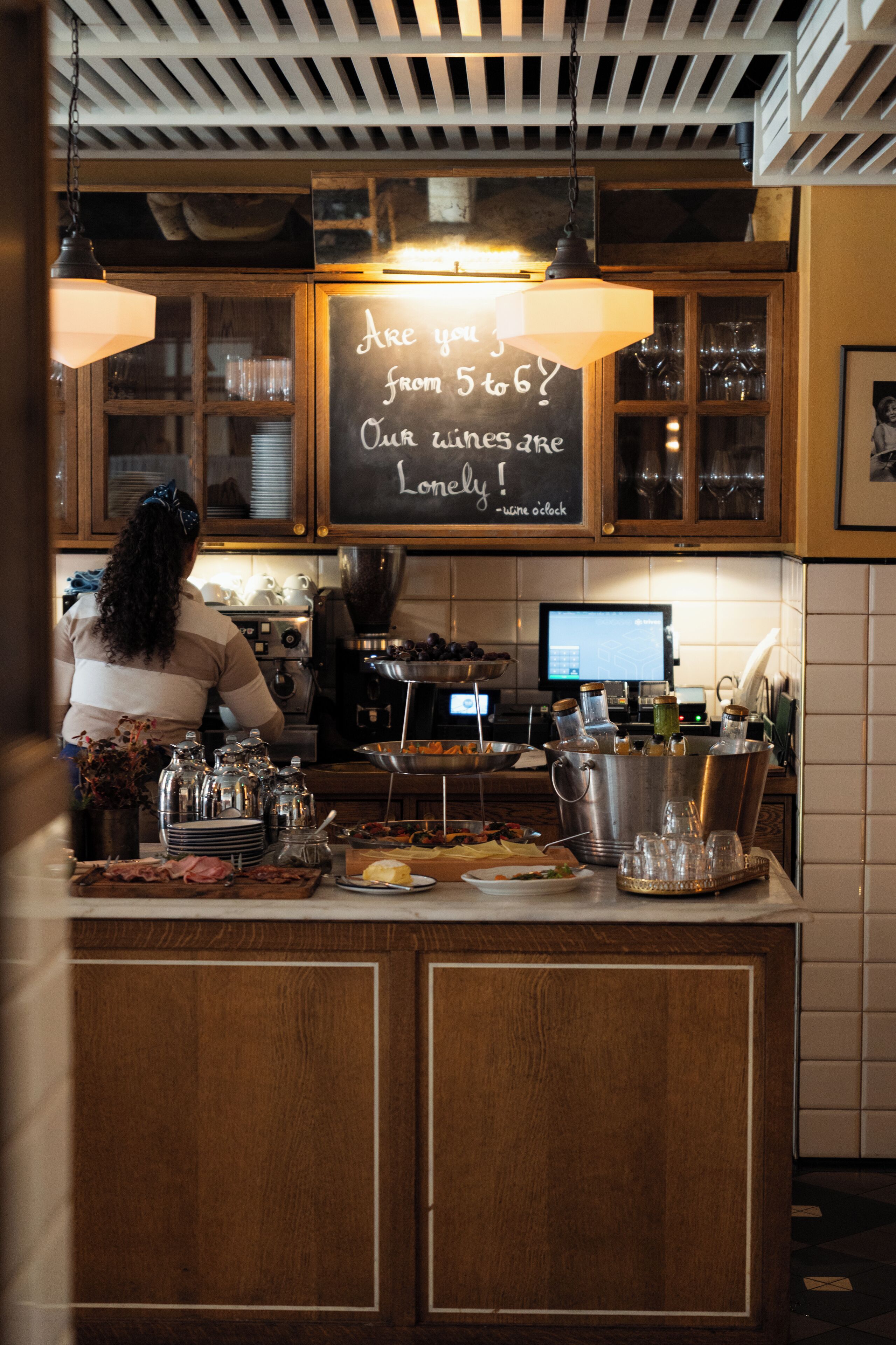 A barista preparing drinks at a counter with a chalkboard sign, coffee machines, and various glassware.
