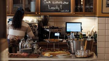 A barista preparing drinks at a counter with a chalkboard sign, coffee machines, and various glassware.