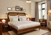 A neatly made bed with a wooden headboard, a bedside table with a lamp, a chair, and a window with curtains.