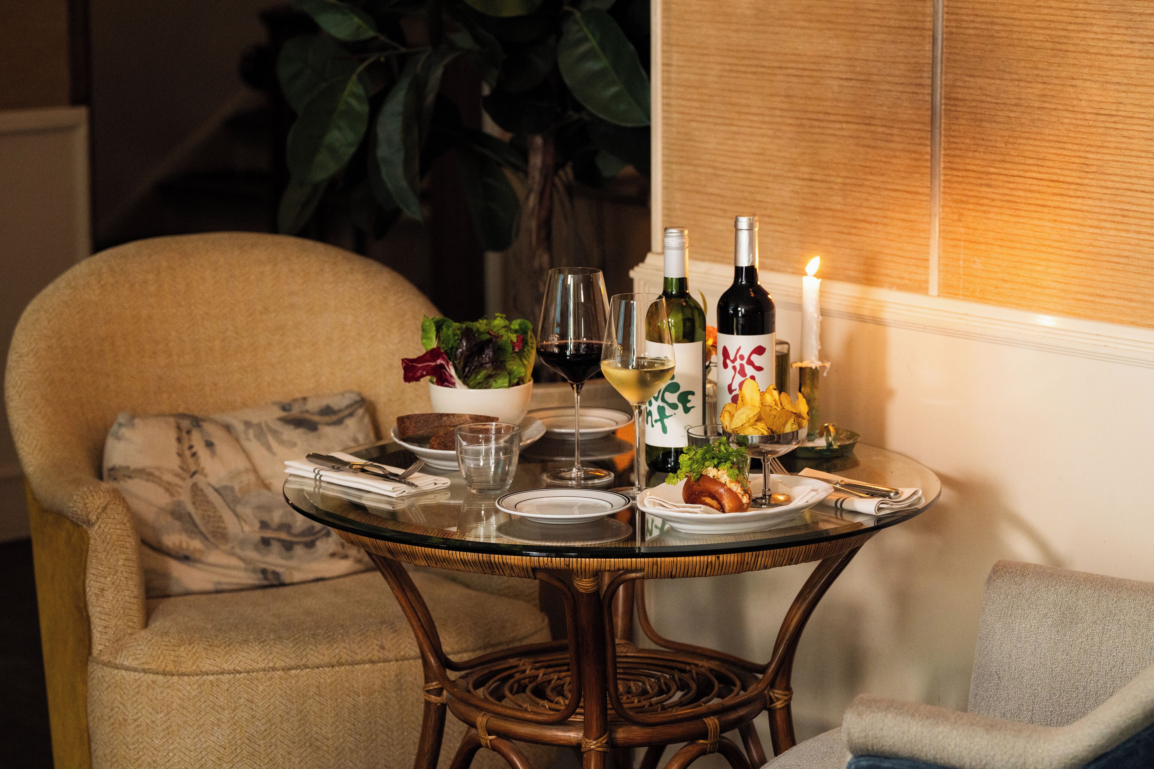 A dining table set with plates, glasses, and bottles, surrounded by chairs.