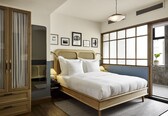 A bedroom with a bed, wooden wardrobe, and a large window.