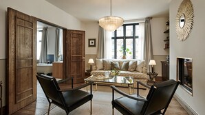 A modern living room with a sofa, two black chairs, a glass coffee table, a chandelier, and a large mirror. - Hotel Sanders (Copenhagen)