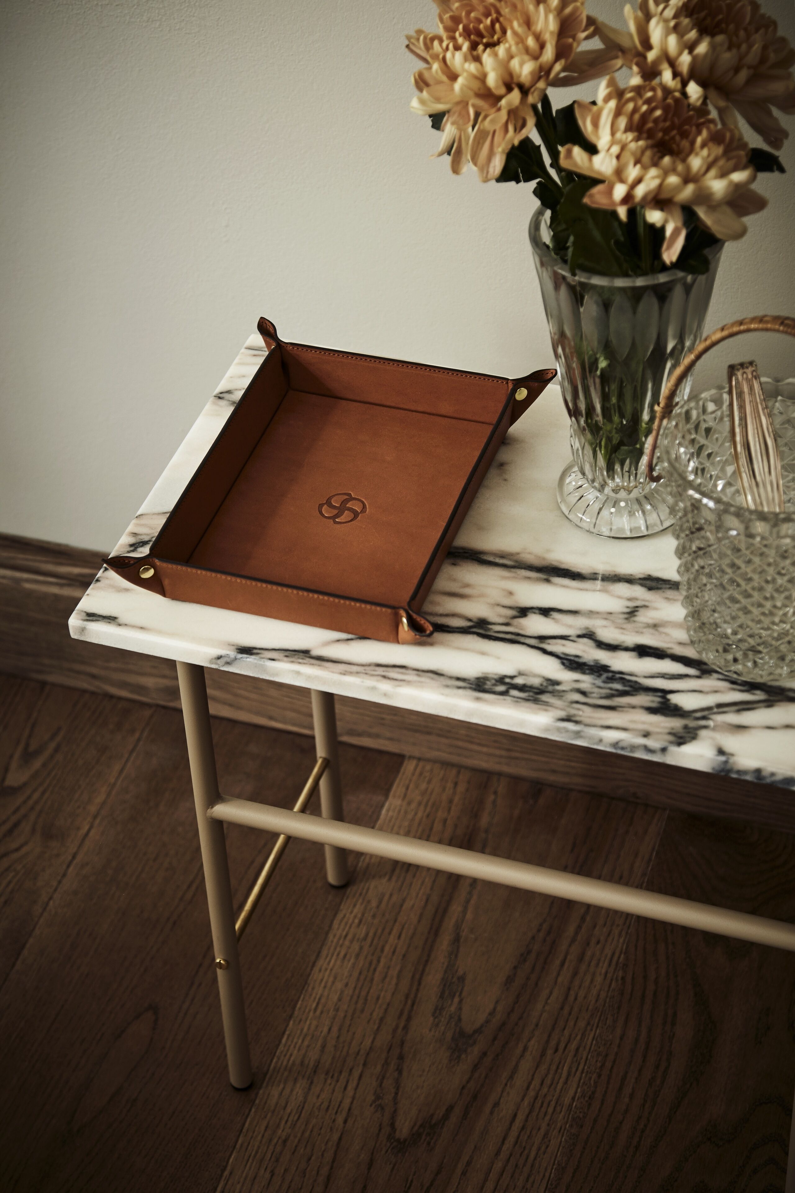 Une table avec un plateau en marbre, un plateau en cuir, un vase avec des fleurs et un récipient en verre contenant une cuillère.