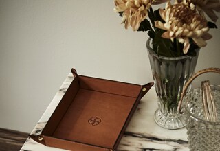 A marble-top table with a leather tray, a vase with flowers, and a glass container with a spoon.