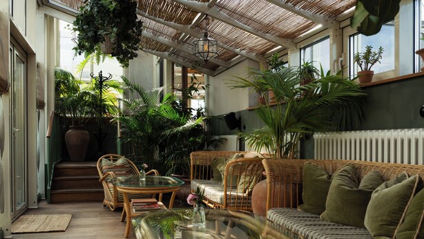 A sunlit room with wicker furniture, a glass coffee table, and various potted plants. - Hotel Sanders (Copenhagen)