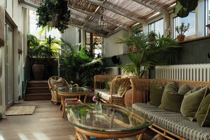 A sunlit room with wicker furniture, a glass coffee table, and various potted plants. - Hotel Sanders (Copenhagen)