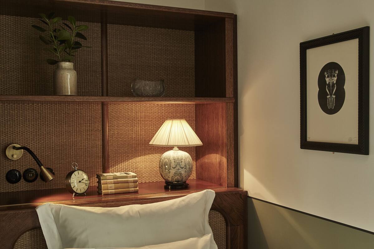 Una estantería de madera bien ordenada con una lámpara, libros, un reloj y un cuadro enmarcado.