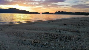 A beach with a calm sea, a boat on the water, and distant hills. - SeeSea Resort (La-ngu)