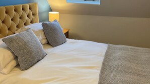 Une chambre à coucher avec un lit, des oreillers, une lampe et une vue sur la mer par la fenêtre.