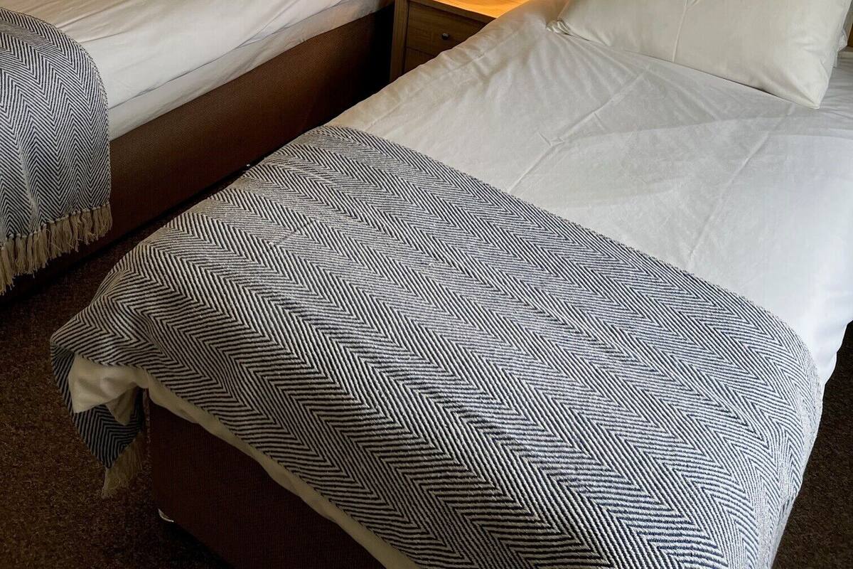 Una habitación de hotel con dos camas, cada una con cabecera, mesita de noche y lámpara.