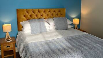Een slaapkamer met een blauwe wand, een houten hoofdbord, een bed met wit en blauw beddengoed en twee nachtlampjes.