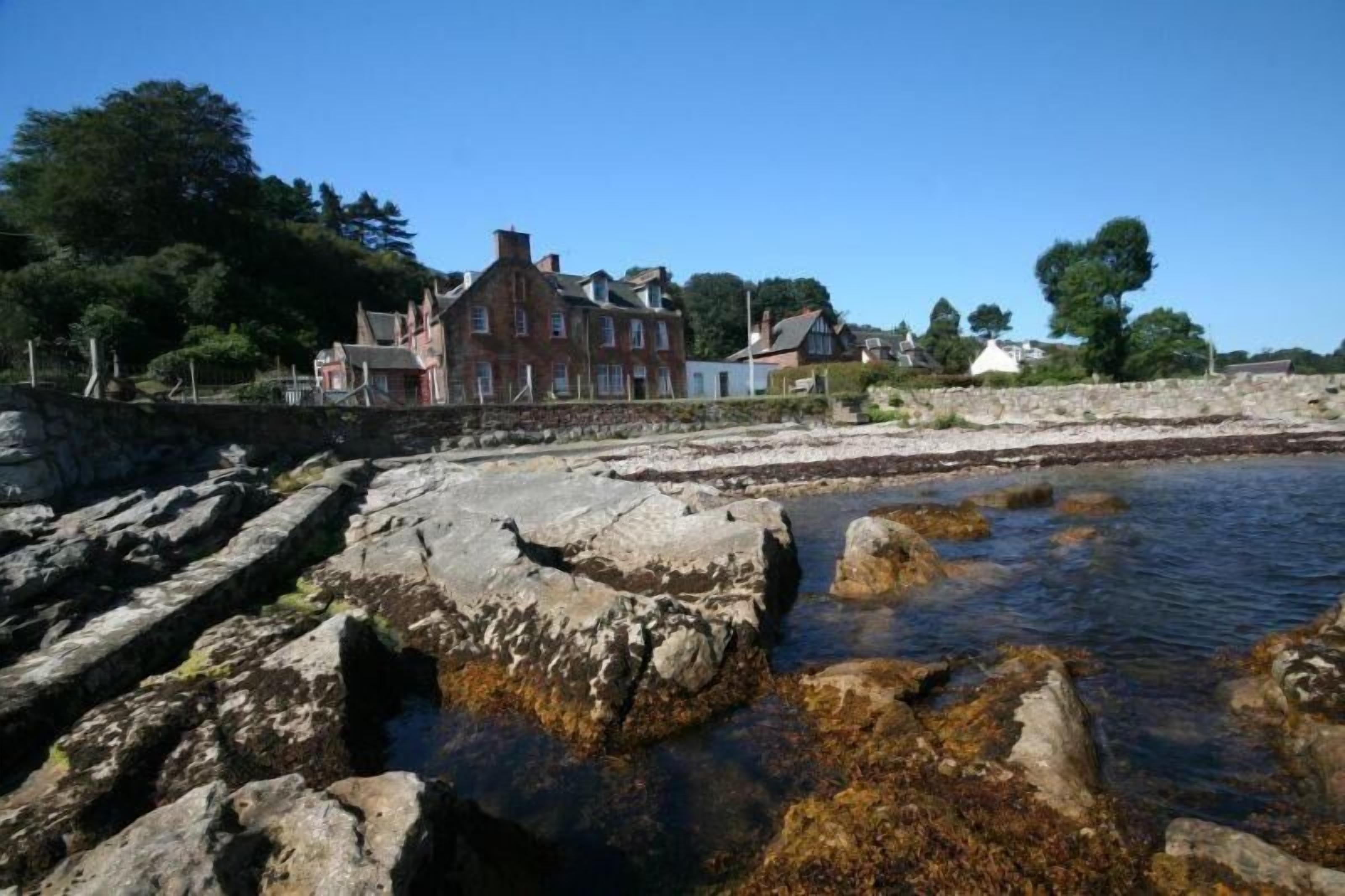 Une zone côtière caractérisée par un grand bâtiment en briques, une côte rocheuse et une eau claire.