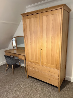 Un armario de madera con dos puertas y un estante en la parte inferior, un escritorio de madera con una silla, y un espejo en la pared.
