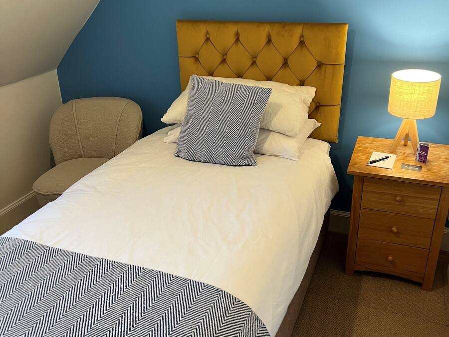 A neatly made bed with a patterned bedspread, a tufted headboard, and a bedside table with a lamp and a book.