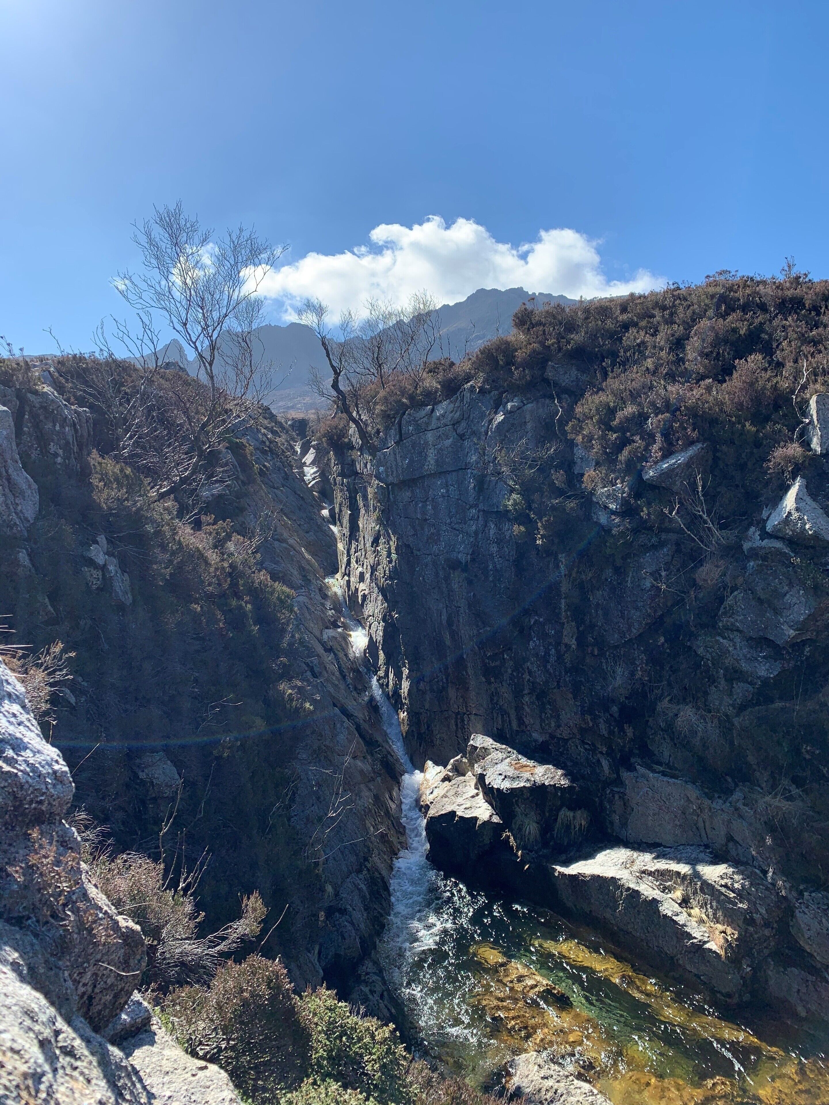 Un cañón con una cascada, terreno rocoso y vegetación escasa.