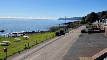 Una carretera costera con mesas de picnic, vista despejada al mar y edificios residenciales.