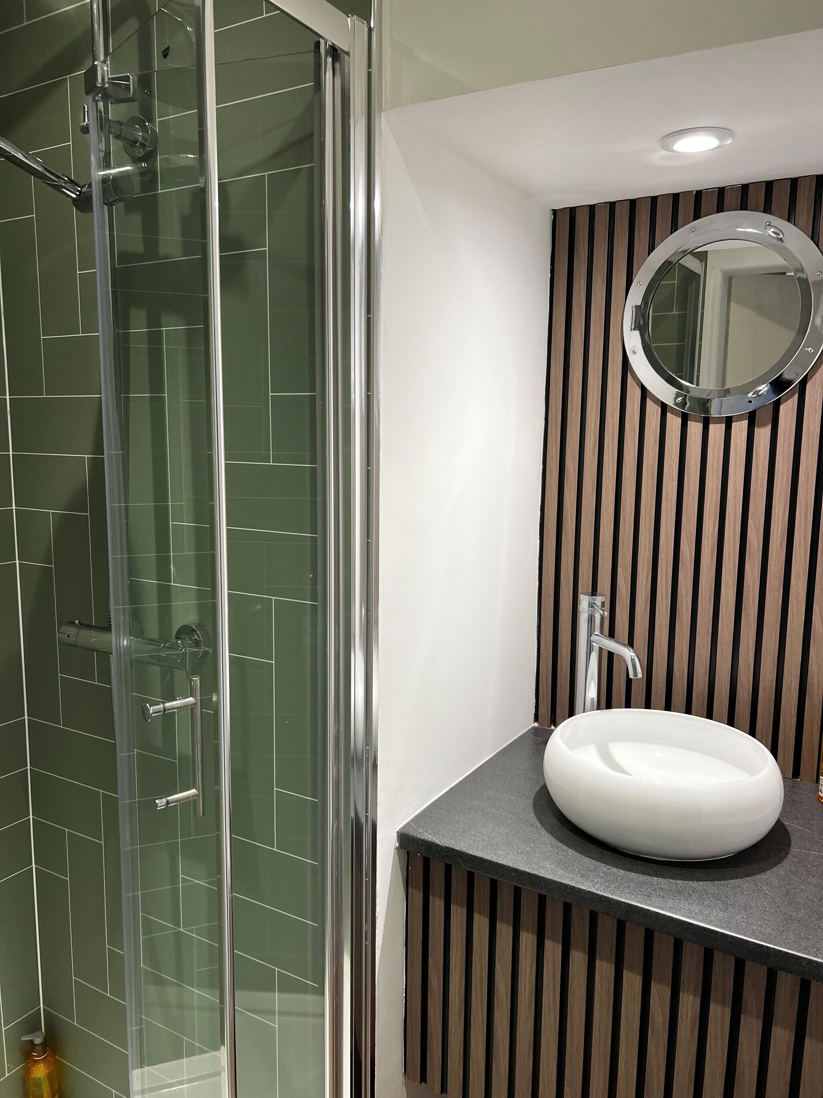 Ein Badezimmer mit Duschkabine aus Glas, einem weißen Waschbecken und einer Wandverkleidung aus Holz.