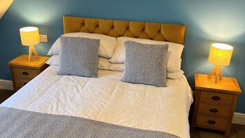 A neatly made bed with a patterned bedspread and two matching pillows, flanked by two bedside tables with lamps, in a room with blue walls and a sloped ceiling.