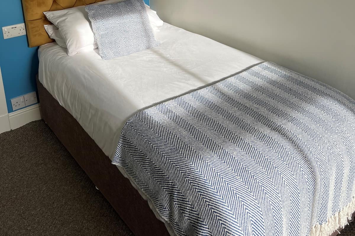 Una cama con cabecera capitonada, ropa de cama blanca y una manta estampada.
