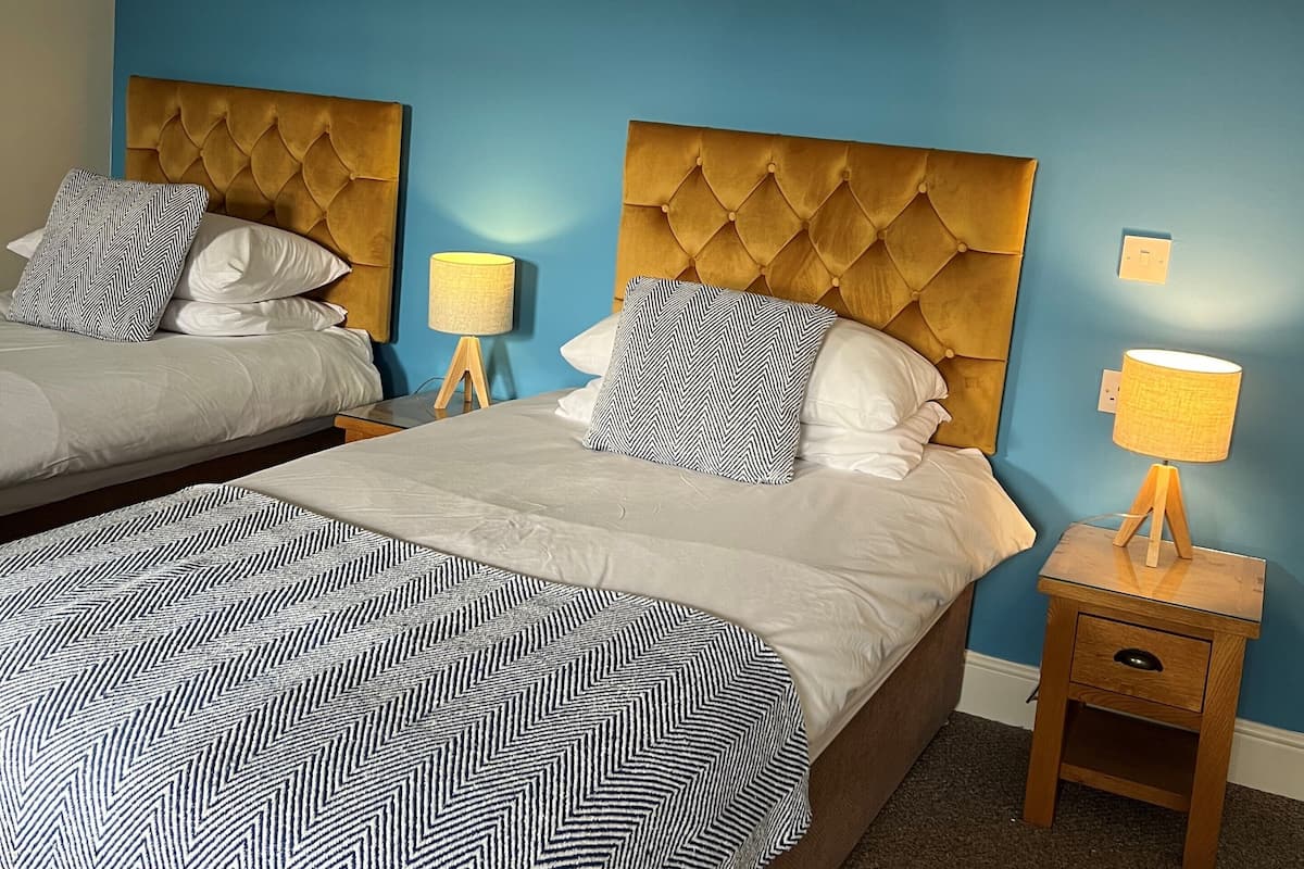 Habitación de hotel con dos camas, cada una con cabecero capitonado, colcha estampada y lámpara de noche.