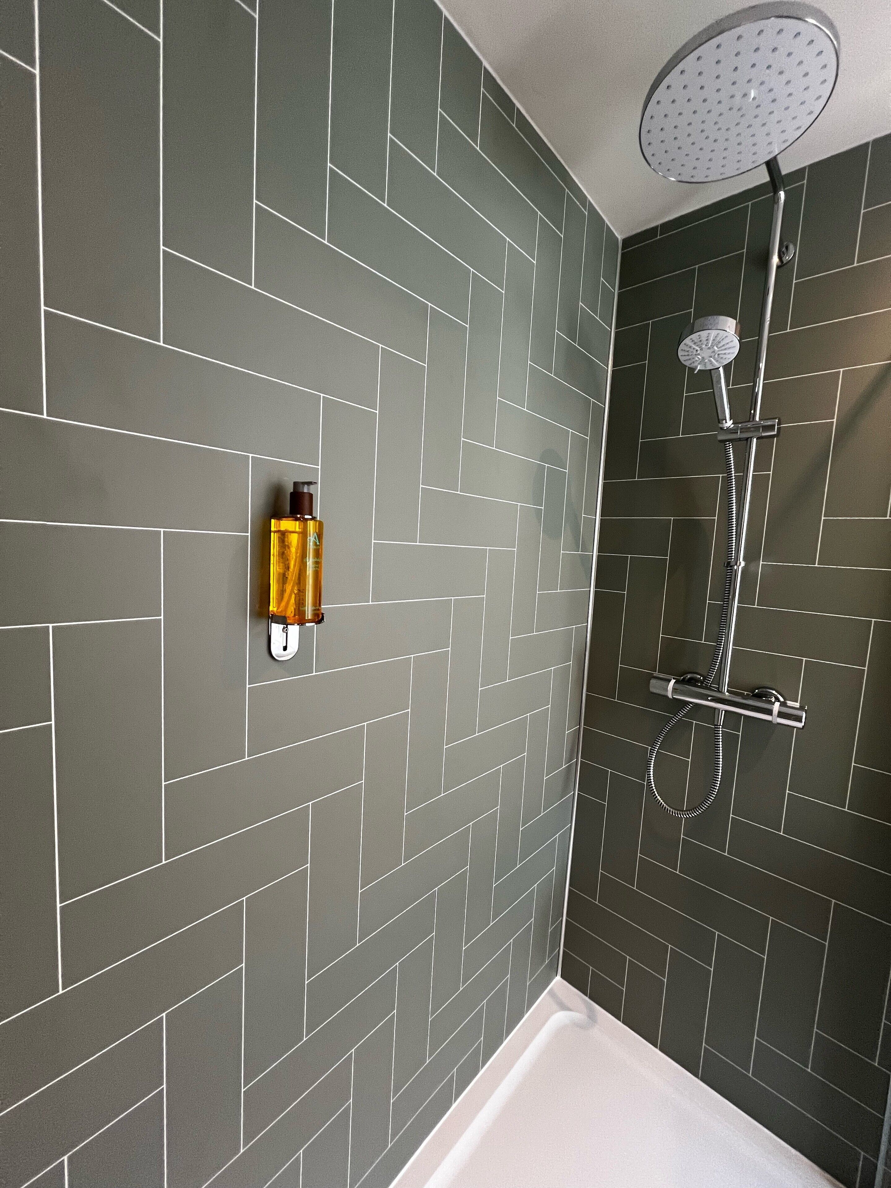 A bathroom with dark grey tiled walls, a white bathtub, and a showerhead.