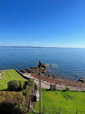 Un paysage côtier comprenant une zone herbeuse, une côte rocheuse et une vue dégagée sur la mer.