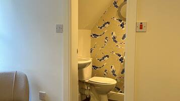 Une salle de bain avec des toilettes, un lavabo et une douche. Il y a une chaise dans la pièce adjacente.
