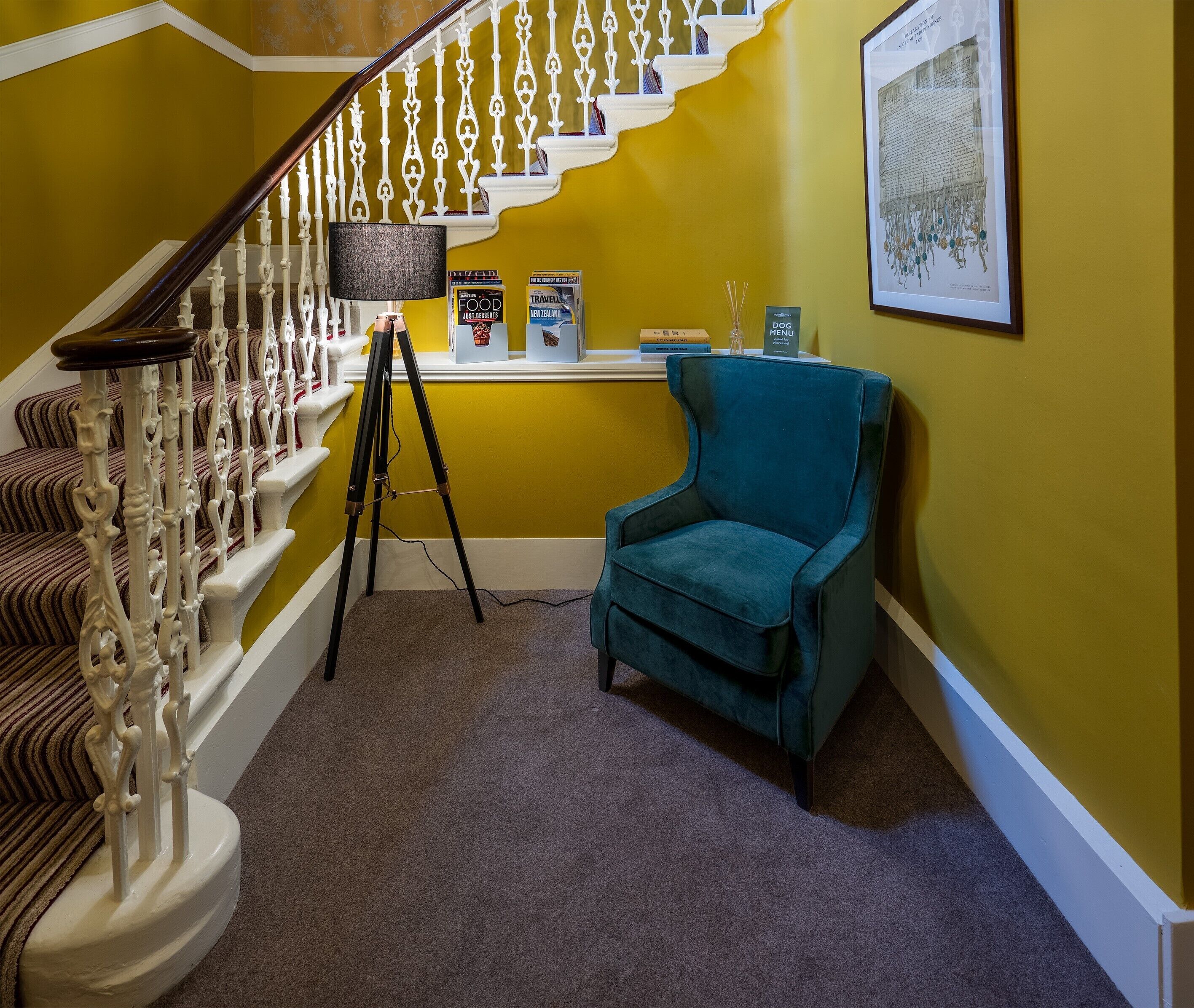 A staircase with ornate white railings, a teal armchair, and a tripod with a camera on the floor.