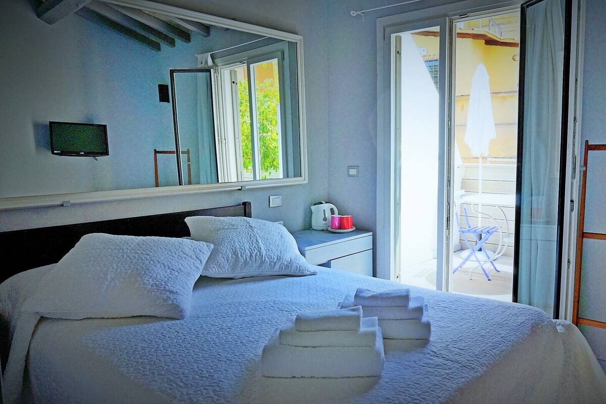 A bedroom with a bed, a bedside table, a mirror, and a sliding glass door leading to an outdoor area.