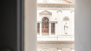 A view through a window of a building with classical architecture, featuring arched windows and decorative moldings. - Buonanotte Colosseo (Rome)