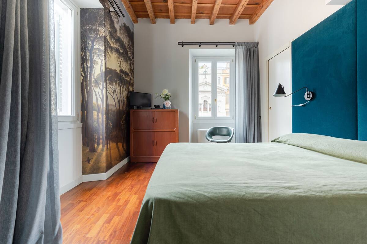 A bedroom with a bed, a dresser, a chair, a TV, and a window with curtains.