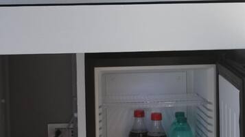 A room with a white-framed mirror, a red mug, and a refrigerator containing beverages and a box of cereal.