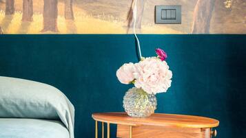 A bedroom with a bed, a wall-mounted lamp, a wooden side table with a vase of flowers, and a power outlet.