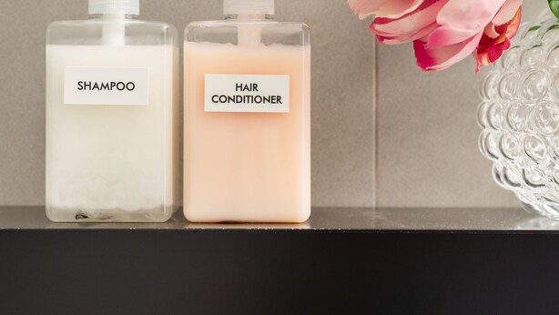 Two bottles of shampoo and hair conditioner on a shelf with a vase of pink flowers. - Buonanotte Colosseo (Rome)
