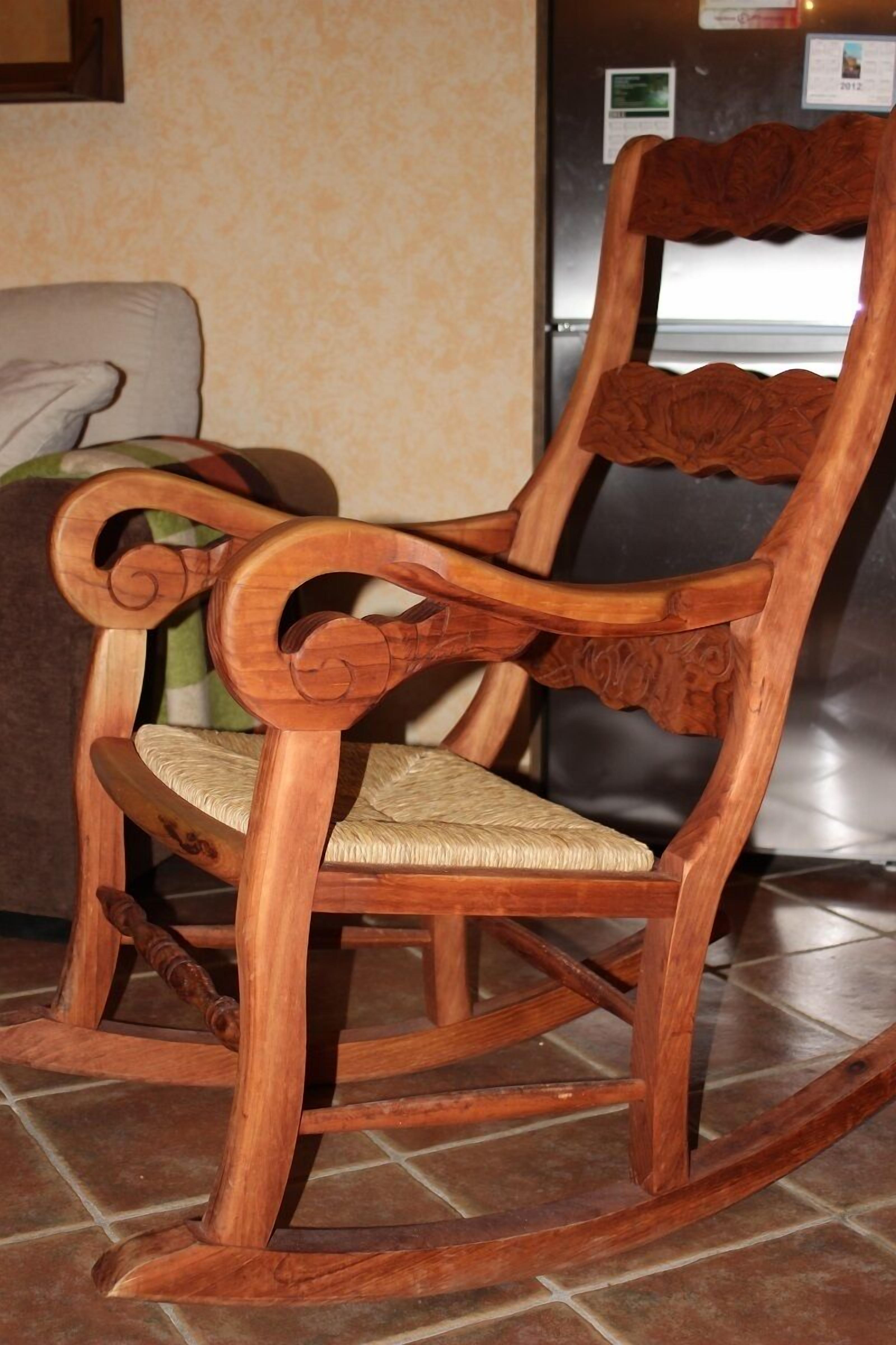 Una mecedora de madera con asiento y respaldo trenzados, ubicada sobre un piso de baldosas.