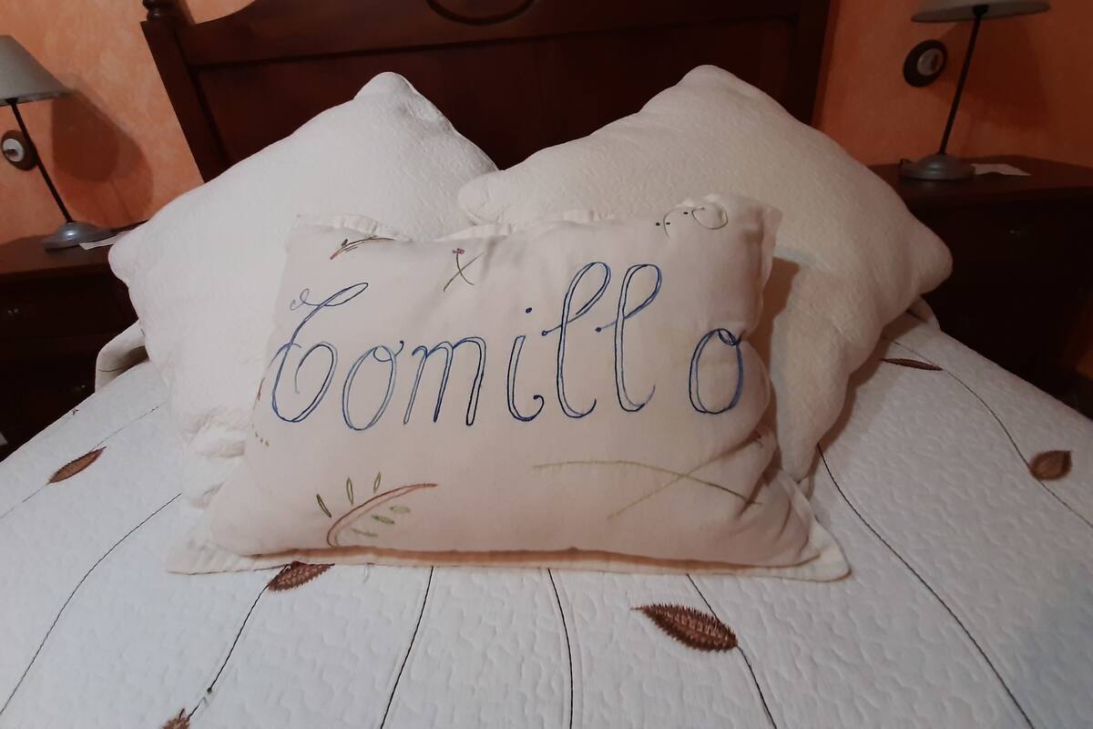 A bed with a white textured bedspread and two pillows, one with the name 'Tomillo' embroidered on it.