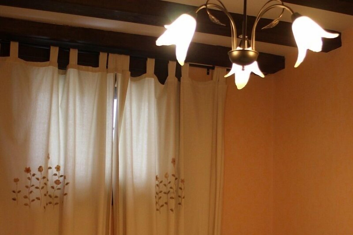 A bedroom with two beds, a wooden headboard, a decorative ceiling light, and a window with curtains.