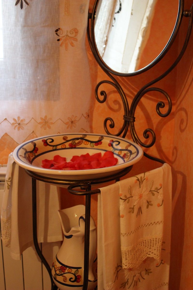 Un baño con un lavamanos blanco, un cuenco decorativo, un espejo y una toalla colgada sobre el lavamanos.