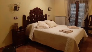 A bedroom with a wooden headboard, a bed with white bedding, a nightstand with a lamp, and a window with curtains. - Apart Rurales Esencias De La Alcarria (Hueva)