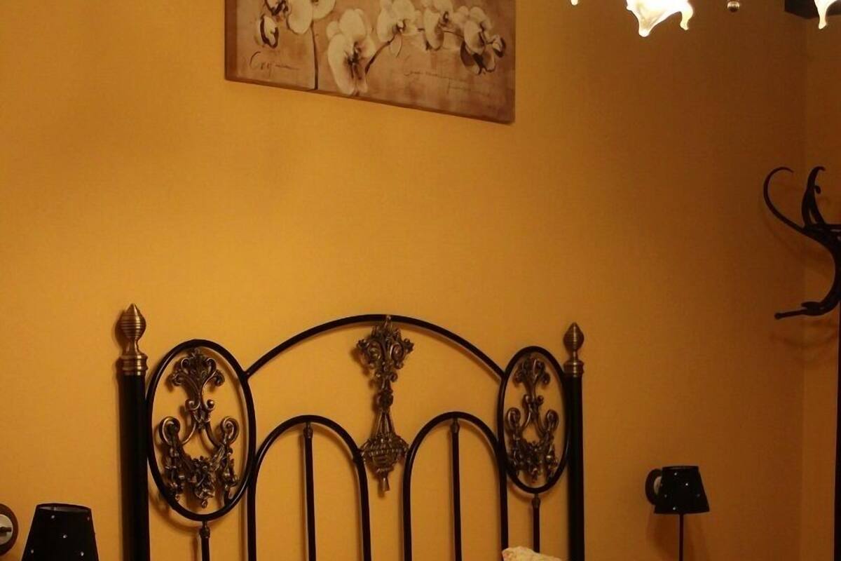 A bedroom with a bed, two bedside tables, a lamp, a wall-mounted artwork, and a decorative metal headboard.