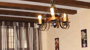 A dining area with a wooden table and chairs, a glass coffee table with a red object, a sofa, and a chandelier. - Apart Rurales Esencias De La Alcarria (Hueva)