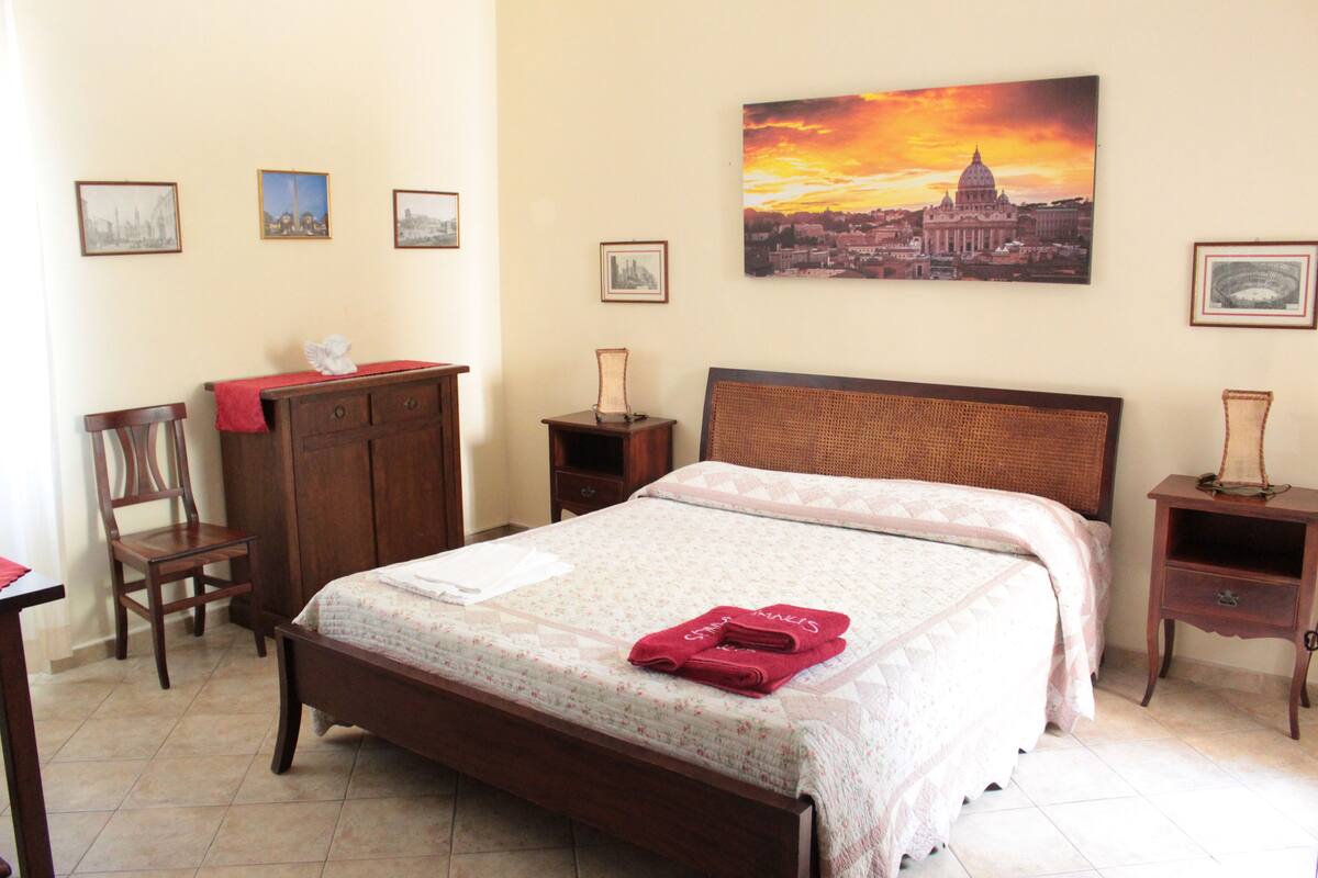 A neatly arranged bedroom with a large bed, a wooden dresser, a chair, and a nightstand.