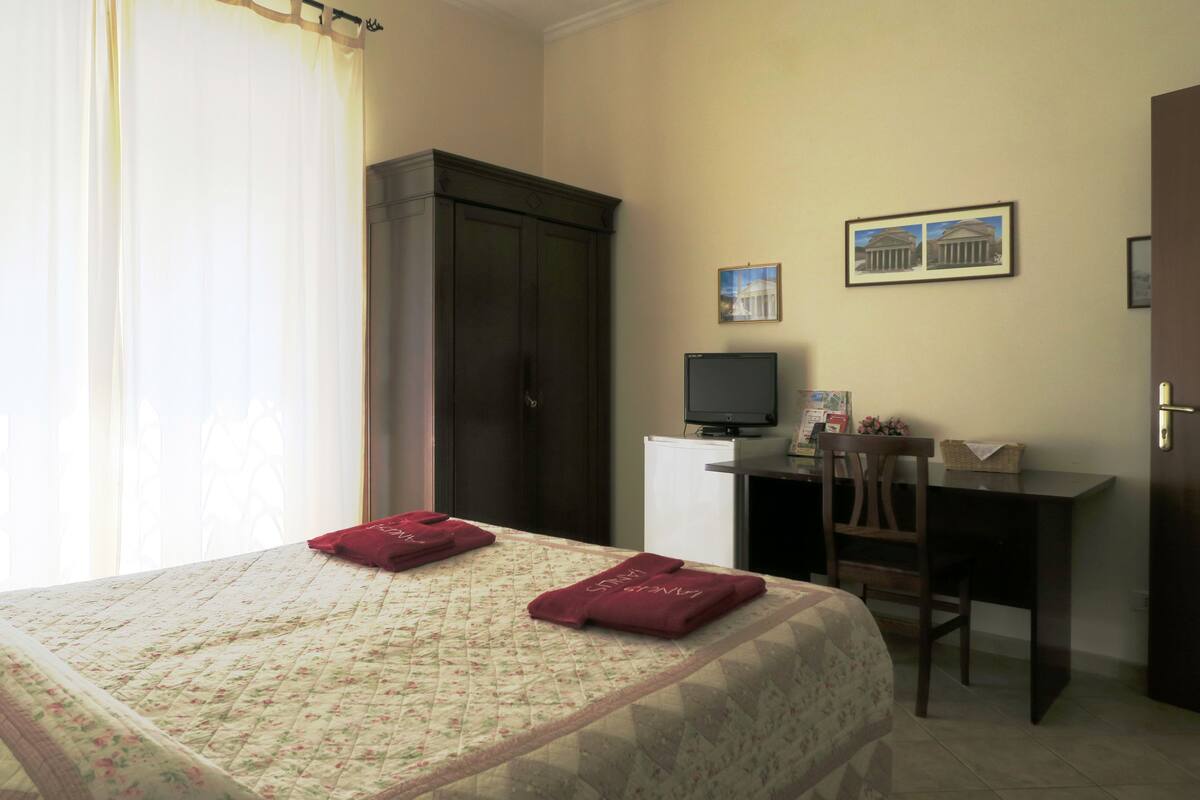 A hotel room with a bed, a desk, a chair, a television, and a wardrobe.