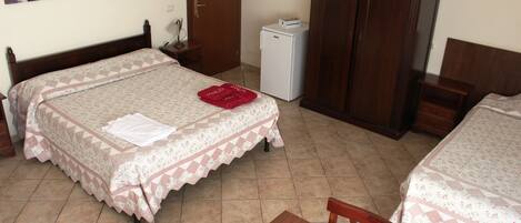 A hotel room with two beds, a small refrigerator, a wooden wardrobe, and a desk with a chair.