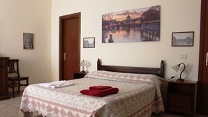 A neatly made bed with a floral bedspread, a red towel, and a painting of a bridge over water on the wall. - Ianus Guest House (Rome)