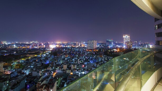A nighttime cityscape with a view of a densely packed urban area, high-rise buildings, and a glass railing overlooking the scene. - Saigon City View Apartment & Pool (Ho Chi Minh City)