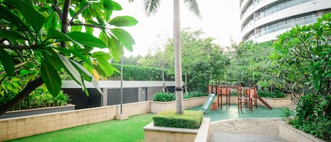 Un patio con un parque infantil, césped verde y una palmera alta.