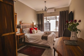 Une chambre à coucher avec un lit, des tables de chevet, un bureau en bois, un vase avec des fleurs et une fenêtre avec des rideaux.