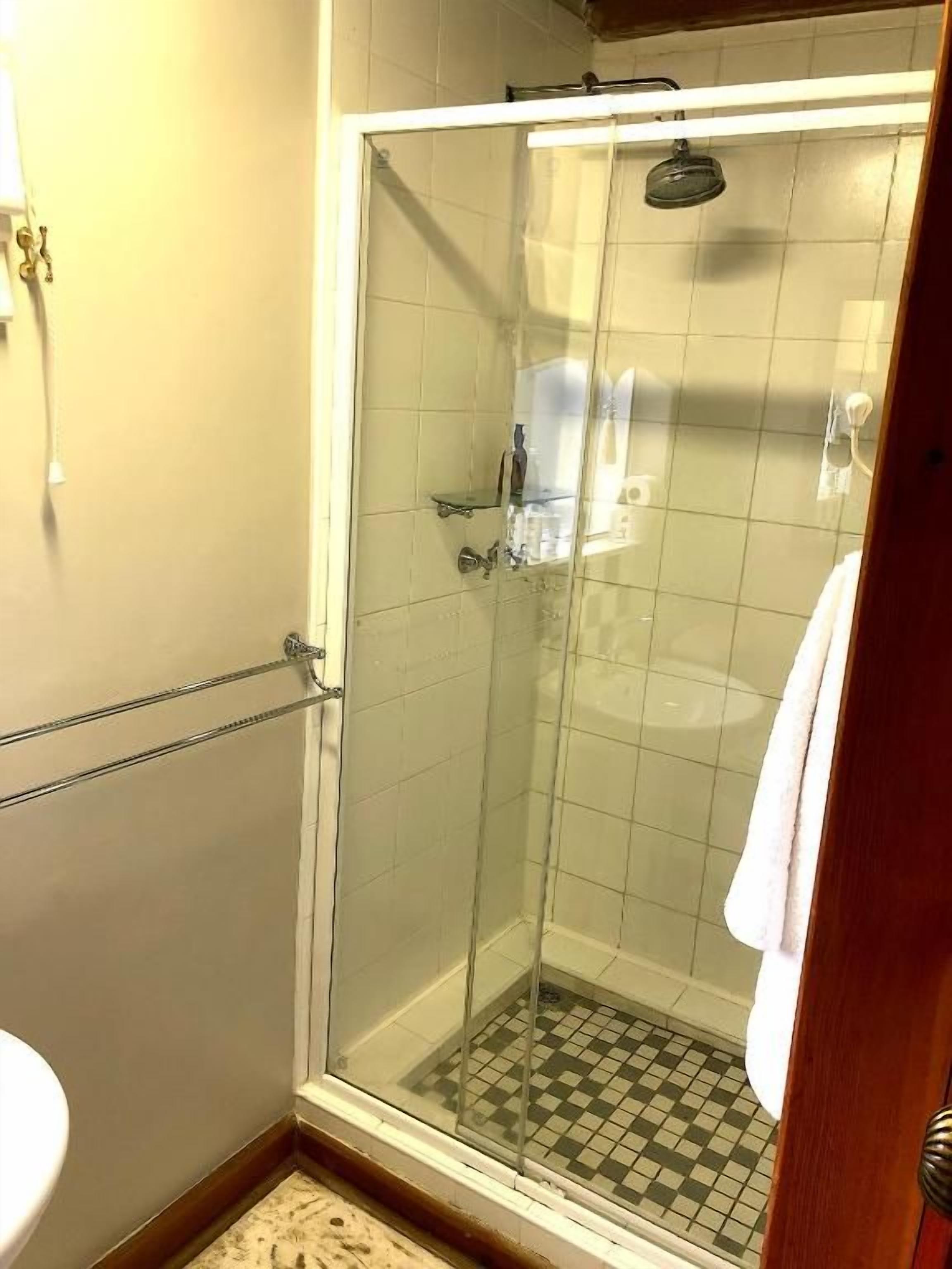 Een douche met glazen wanden, een geruit vloertje, een witte handdoek aan de deur en een zichtbare douchekop.