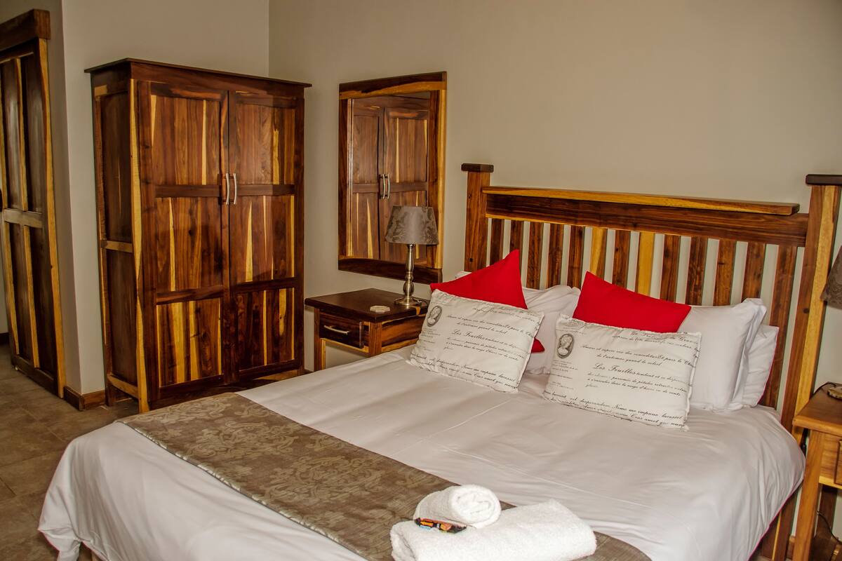 A neatly made bed with white linens and red pillows, a wooden headboard, and a wooden wardrobe beside it.